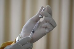 Healthcare worker in gloves drawing a vaccine from a vial into a syringe