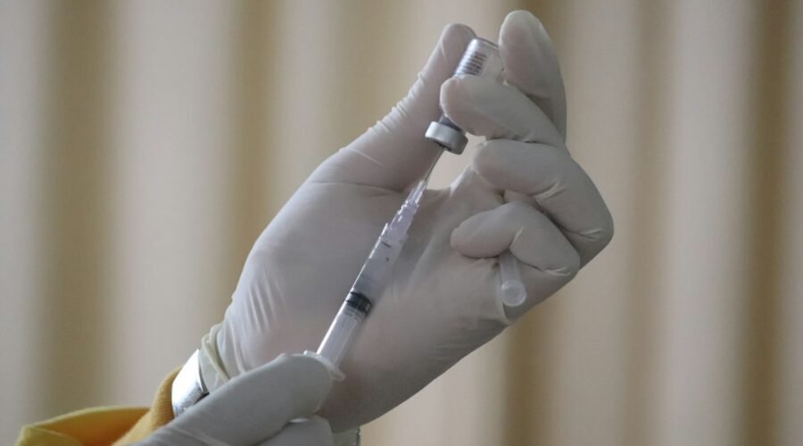 Healthcare worker in gloves drawing a vaccine from a vial into a syringe